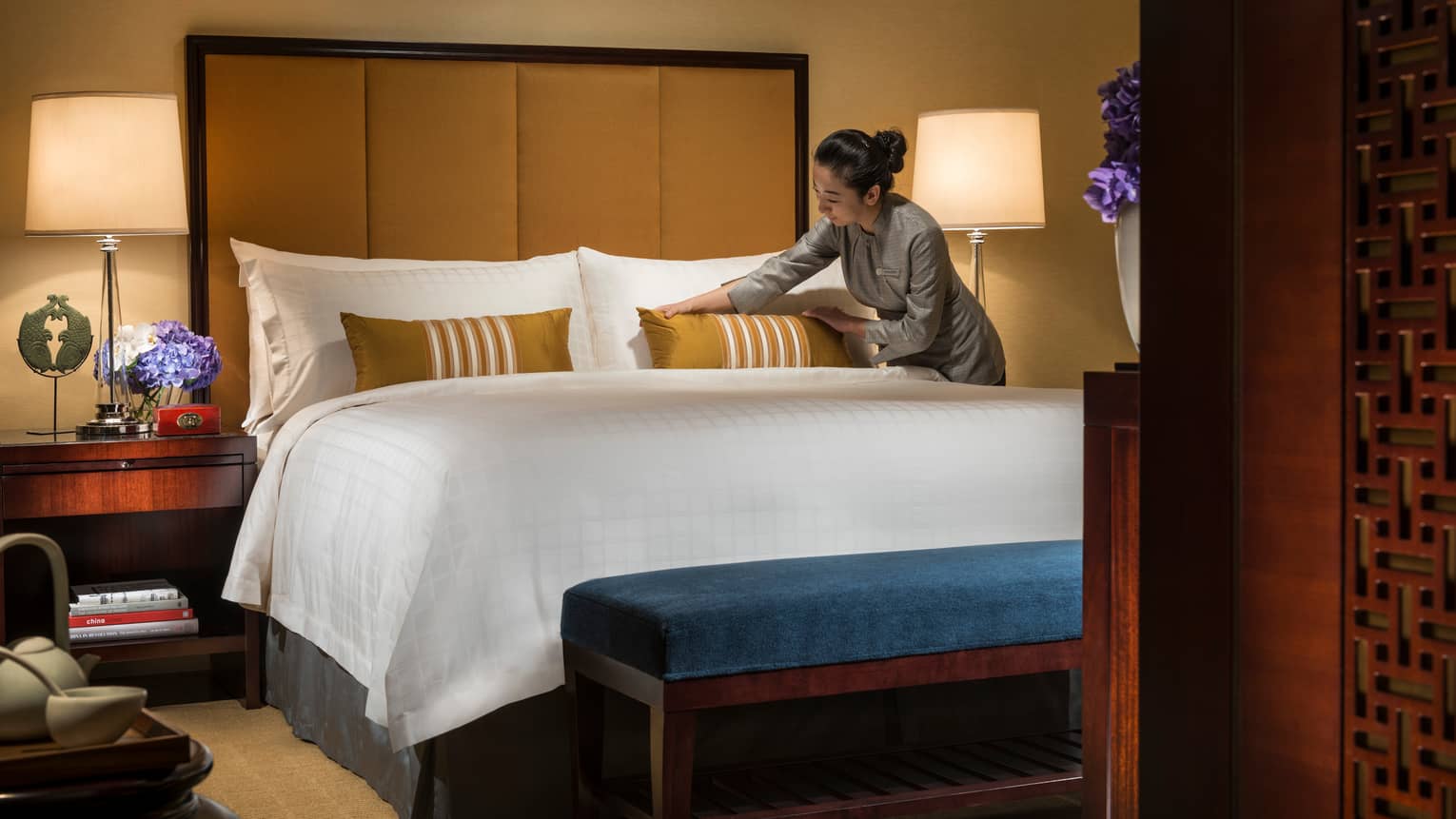 Hotel staff makes bed, adjusts gold accent pillow on white pillows, linens