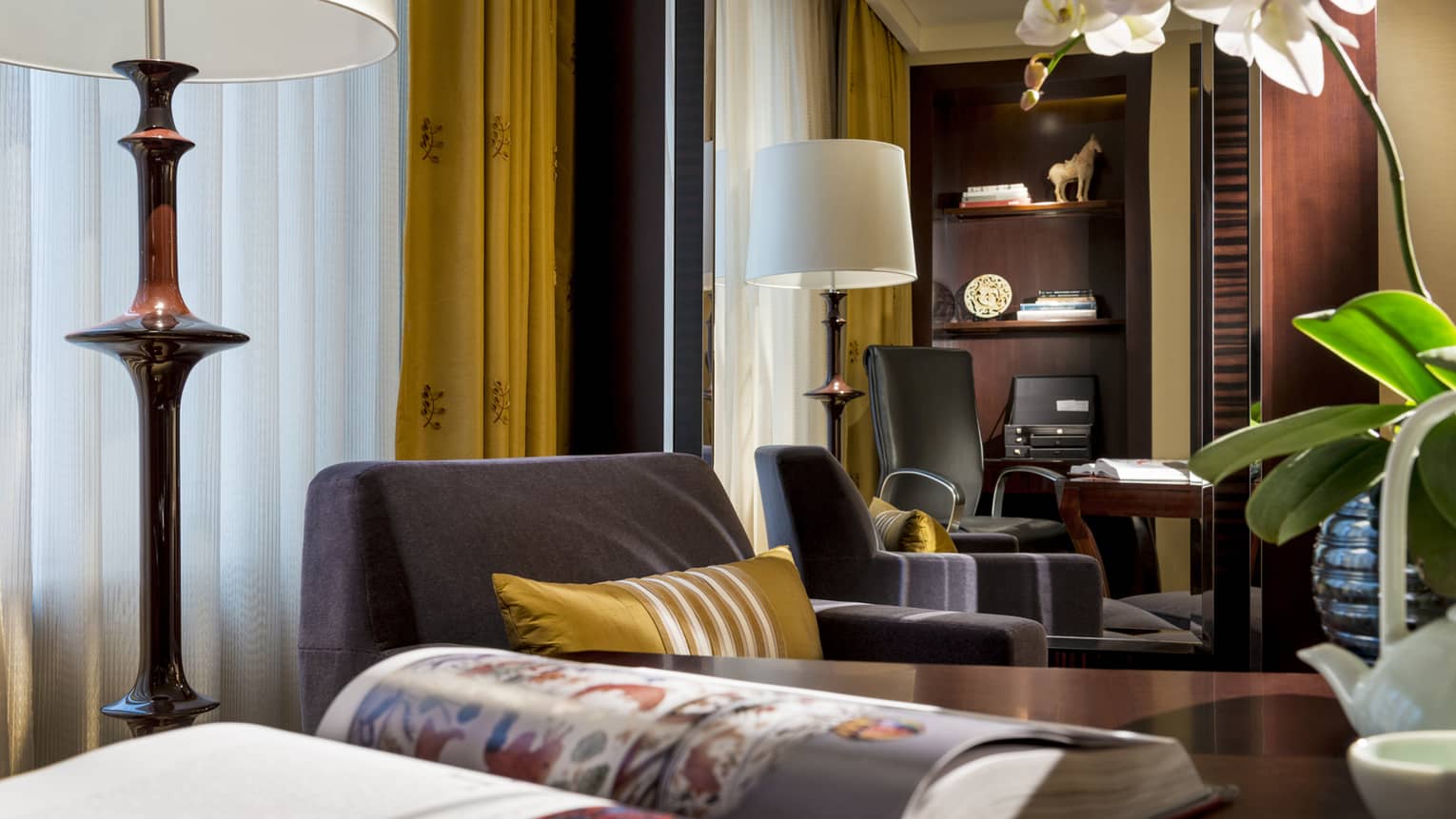 Club Room close-up of tall lamp, white orchid, plush armchairs, gold accent pillow in front of mirror