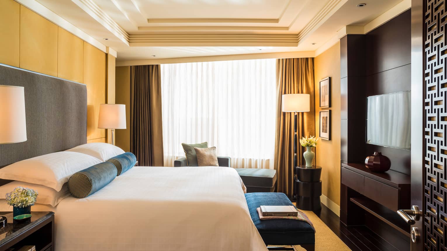 Side view of Beijing Suite bed, bench in front of wood panel wall, chaise by curtains