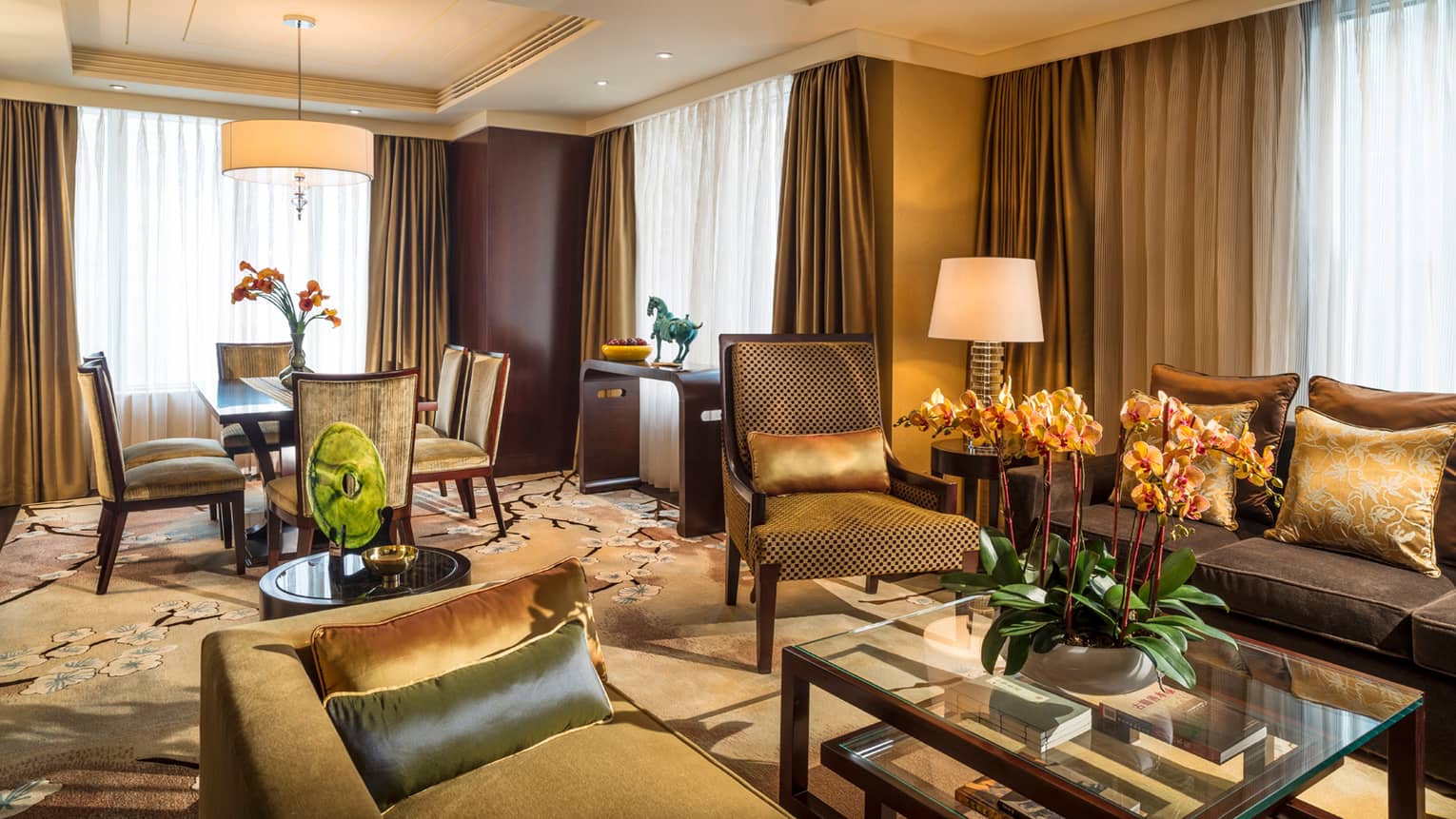 Chairman Suite living room with gold and green sofas and accent pillows, carpet, dining table, curtains on corner windows