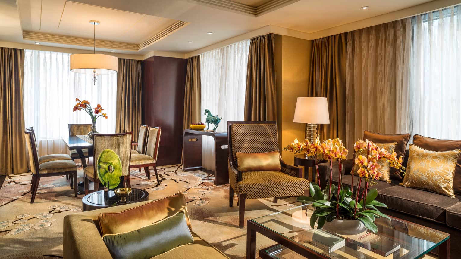 Chairman Suite living room with gold and green sofas and accent pillows, carpet, dining table, curtains on corner windows