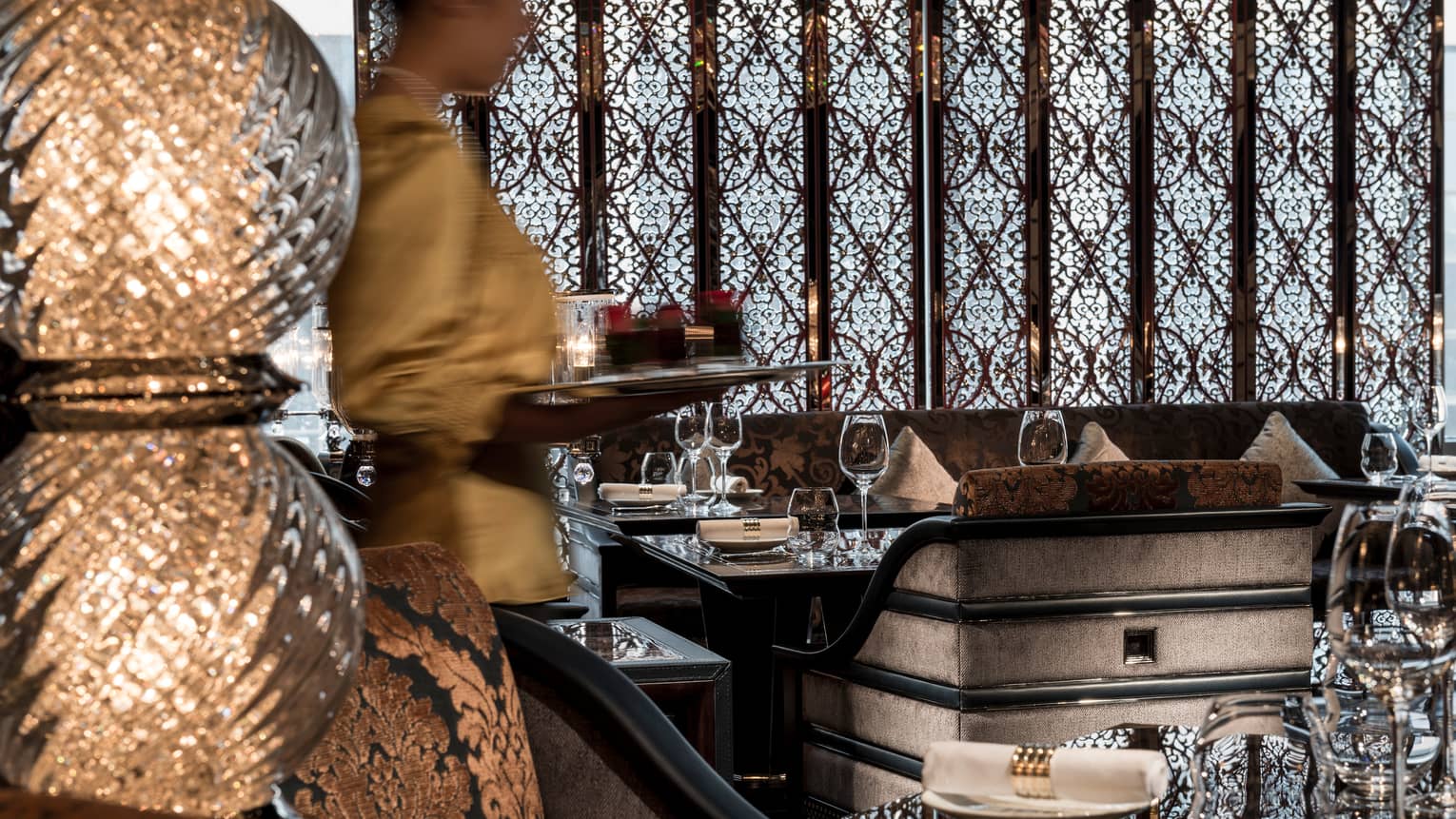 Tall glass lamp in front of server with tray, elegant grey upholstered dining chair, decorative screen on wall