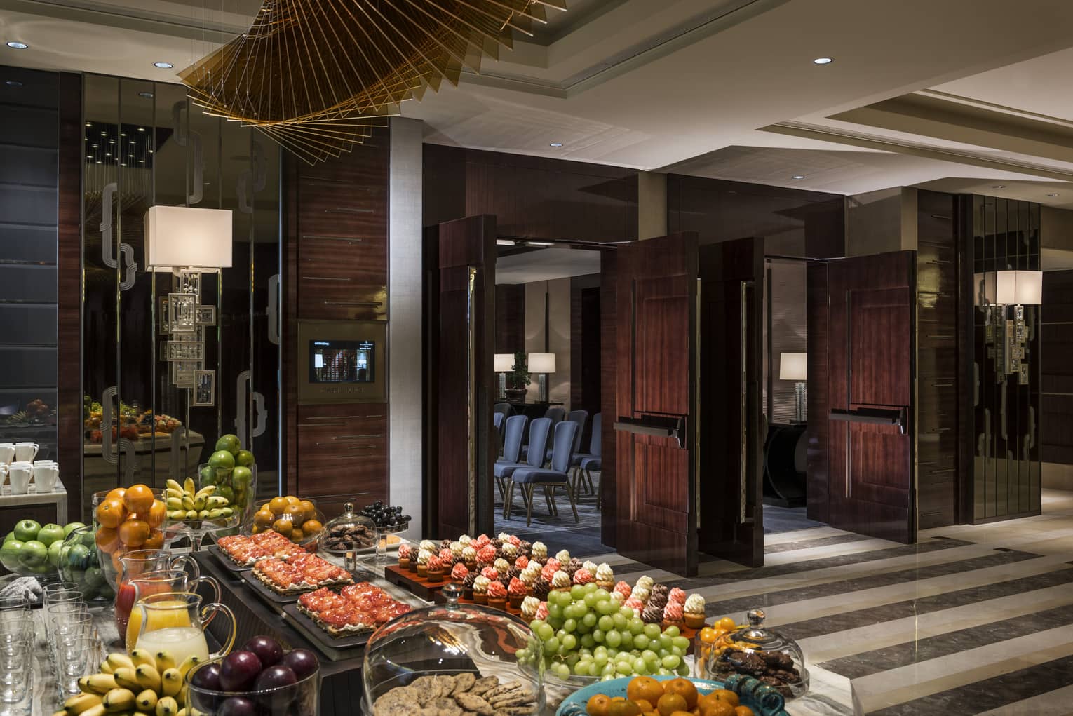 Large buffet table with bowls of fresh fruit, trays with cupcakes in lobby