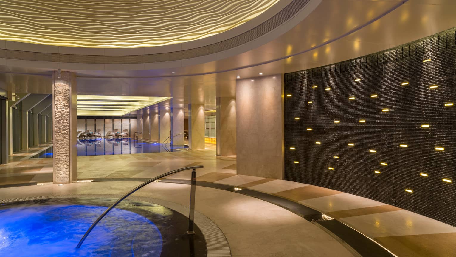 Blue water, stairs of indoor whirlpool, swimming pool in background