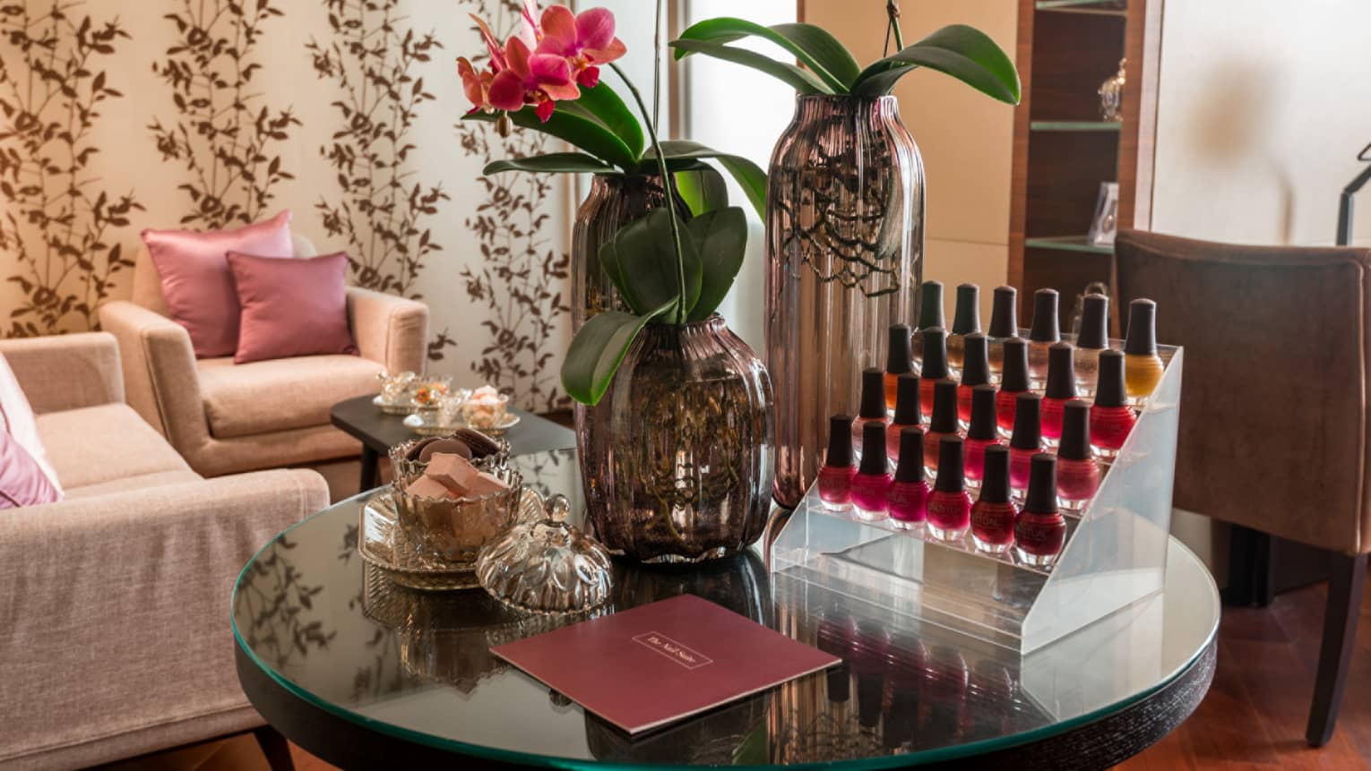 Close-up of The Nail Suite round table with trays of nail polish, flowers in vase